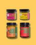 Indisches BBQ Set von Karma Food mit Gewürzen und Saucen: BBQ Masala, Golden Salt, Chili Mango Sauce und Kashmiri Chili Crisp in bunten Gläsern vor gelbem Hintergrund