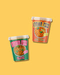 Zwei Becher von Karma Food mit Bio Spinat Linsen Dal und Bio Tikka Masala Curry auf gelbem Hintergrund