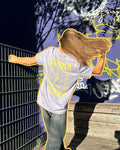 Frau trägt ein weißes Korma-Curry-T-Shirt von Karma Food vor Graffiti-Wand