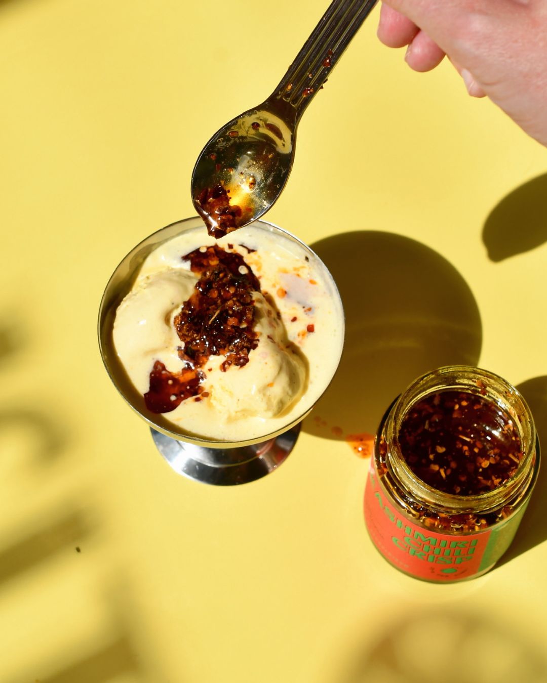Kashmiri Chili Crisp wird mit einem Löffel über cremiges Vanilleeis geträufelt – kreative Kombination aus Schärfe und Süße, Sommerdessert von Karma Food.