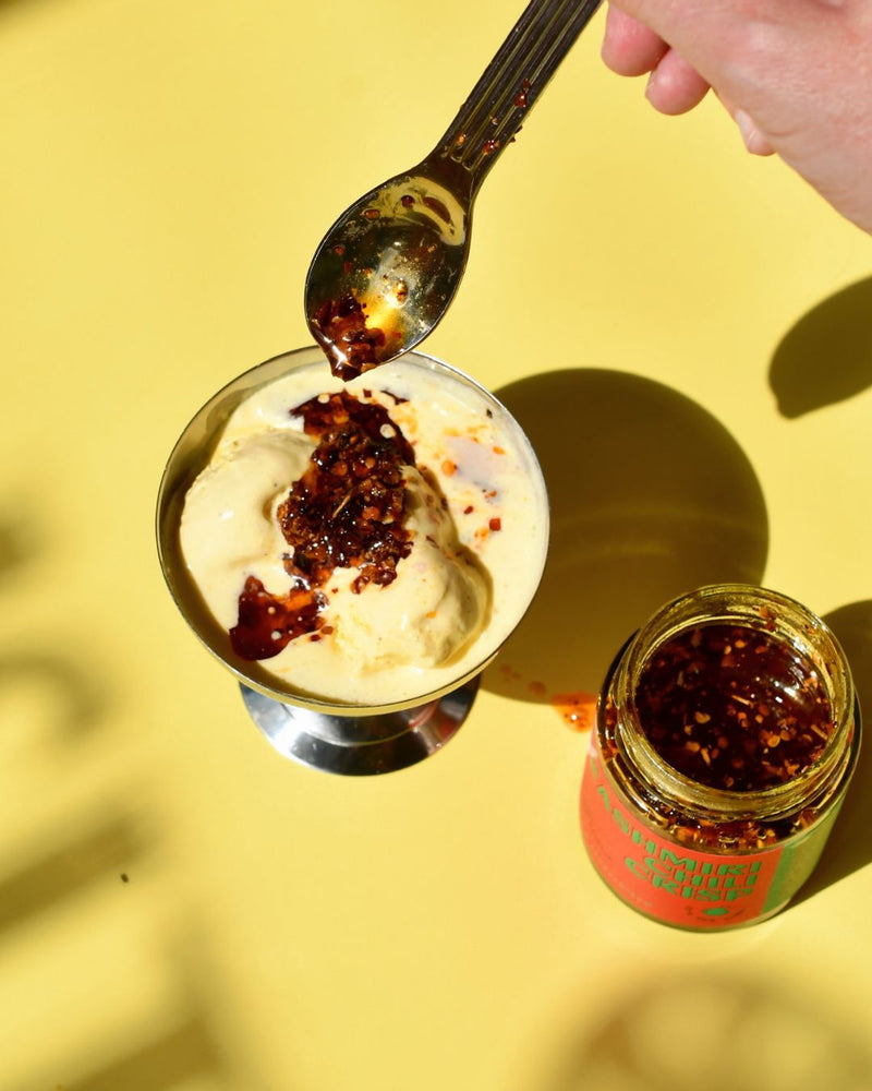 Kashmiri Chili Crisp wird mit einem Löffel über cremiges Vanilleeis geträufelt – kreative Kombination aus Schärfe und Süße, Sommerdessert von Karma Food.