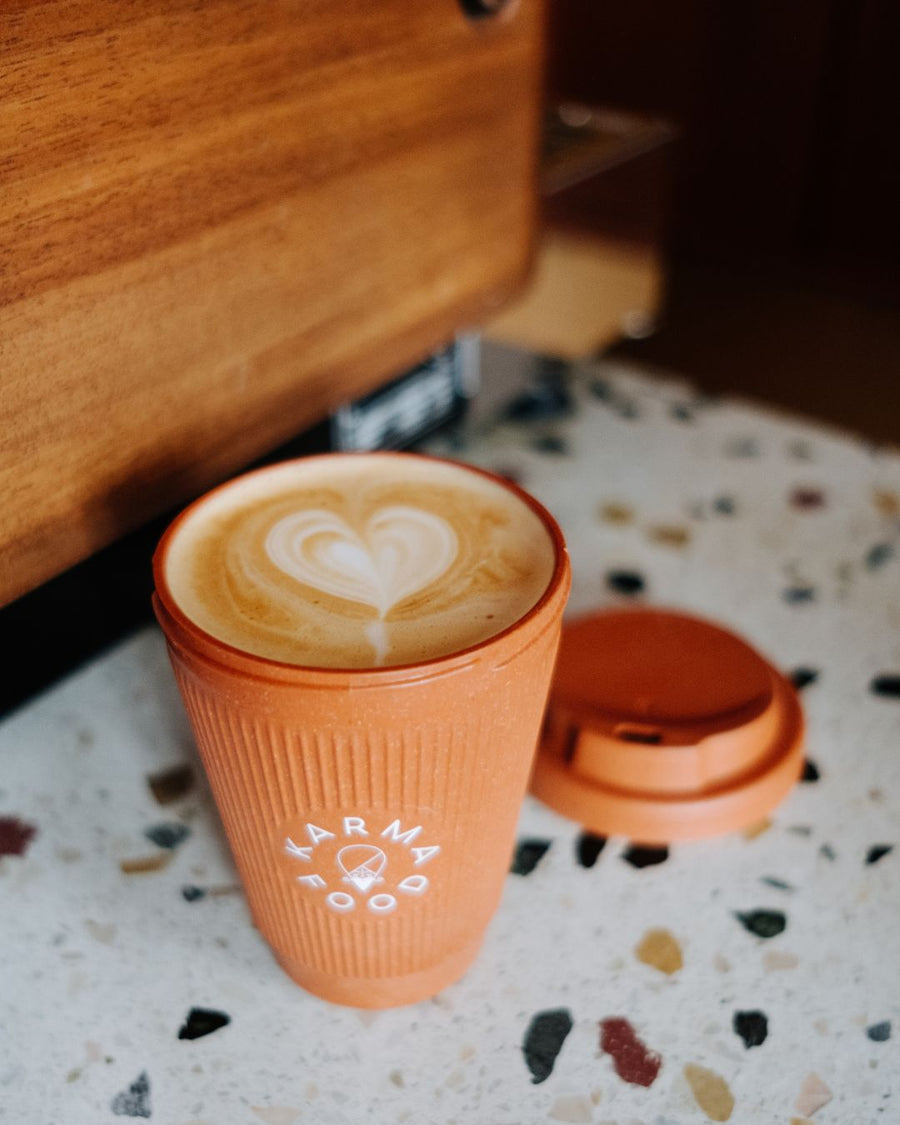 Frischer Latte mit Herzmotiv im Weducer Cup von Karma Food, auf einem Terrazzo-Tisch im Café