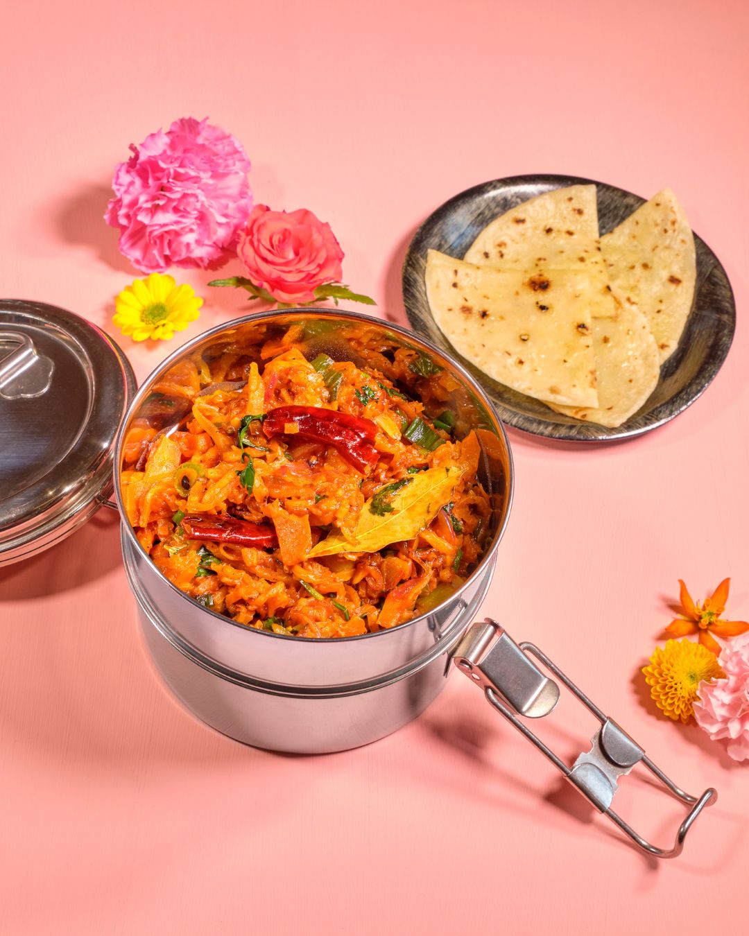 Indisches Curry-Gemüse in einer Edelstahlbox mit Chapati-Fladenbrot auf pinkem Hintergrund
