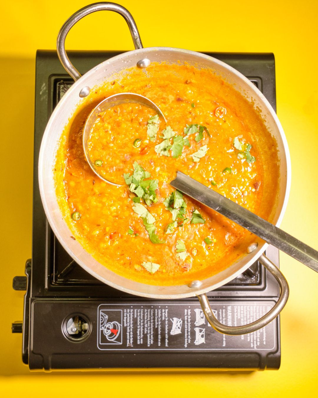 Indisches Dal in einer silbernen Pfanne auf einem gelben Hintergrund, verfeinert mit frischem Koriander