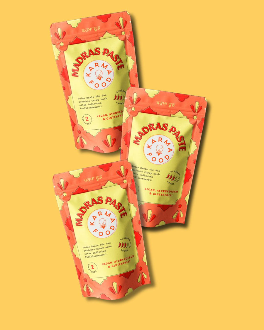 Drei Packungen Madras Curry Paste von Karma Food auf gelbem Hintergrund, vegan und glutenfrei


